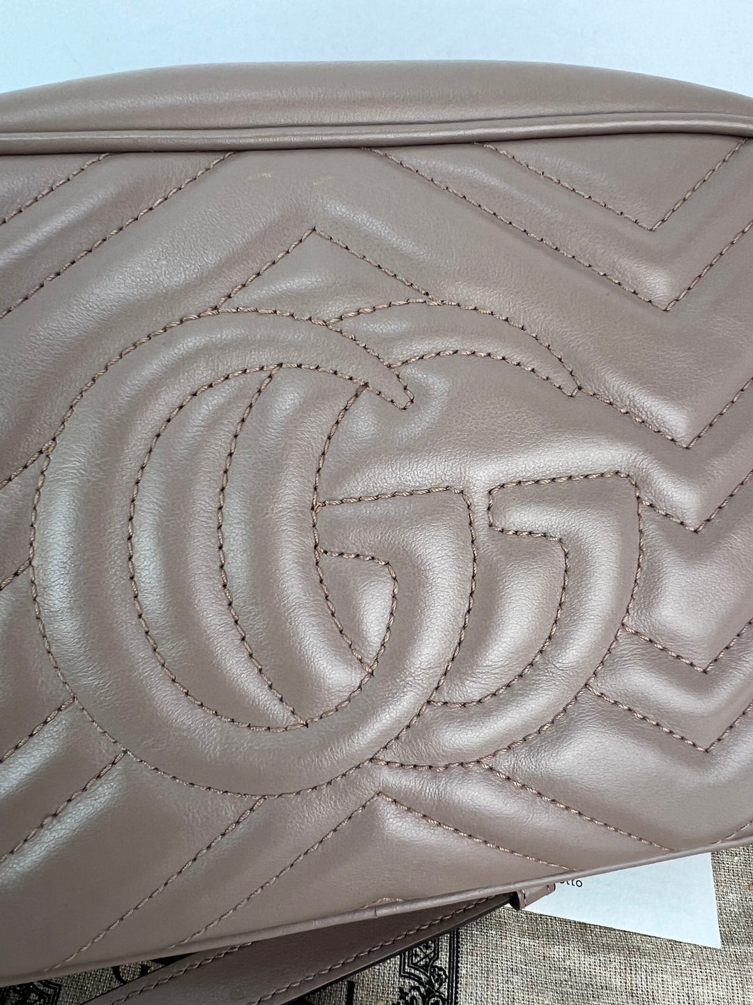 Close-up of a beige handbag with a prominent logo on a light blue background