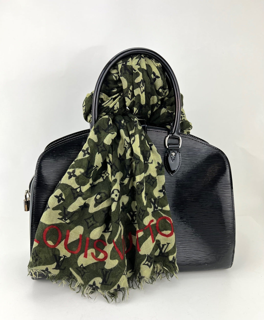Black handbag with a green camouflage-style scarf draped over it on a white background