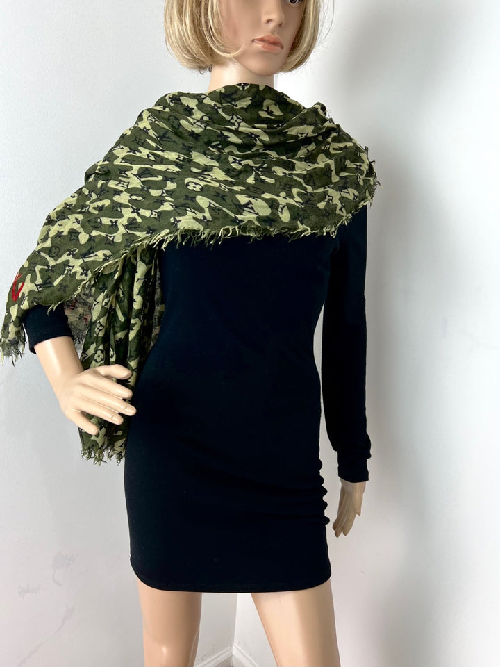 Mannequin wearing a black dress with a green camouflage scarf on a white background