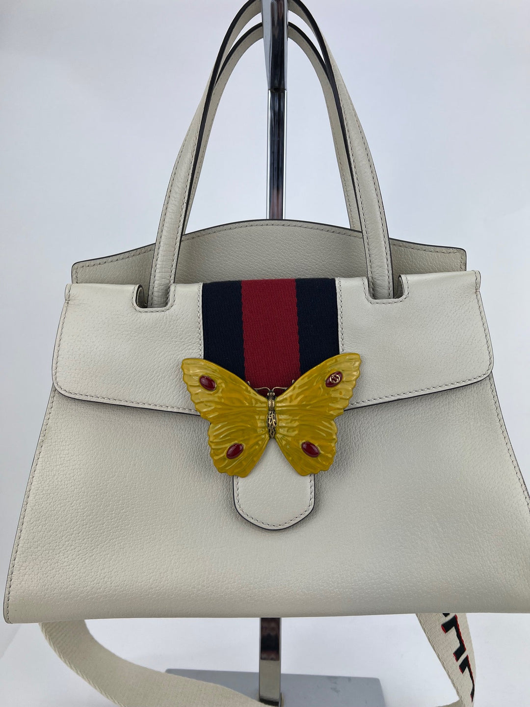 White handbag with a butterfly emblem and colorful stripe on a white background