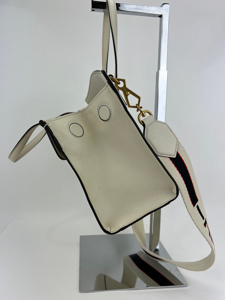 Beige handbag with a strap on a metal stand against a white background