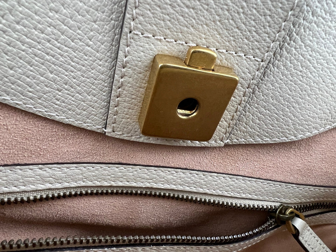 Close-up of a gold clasp on a light-colored leather bag