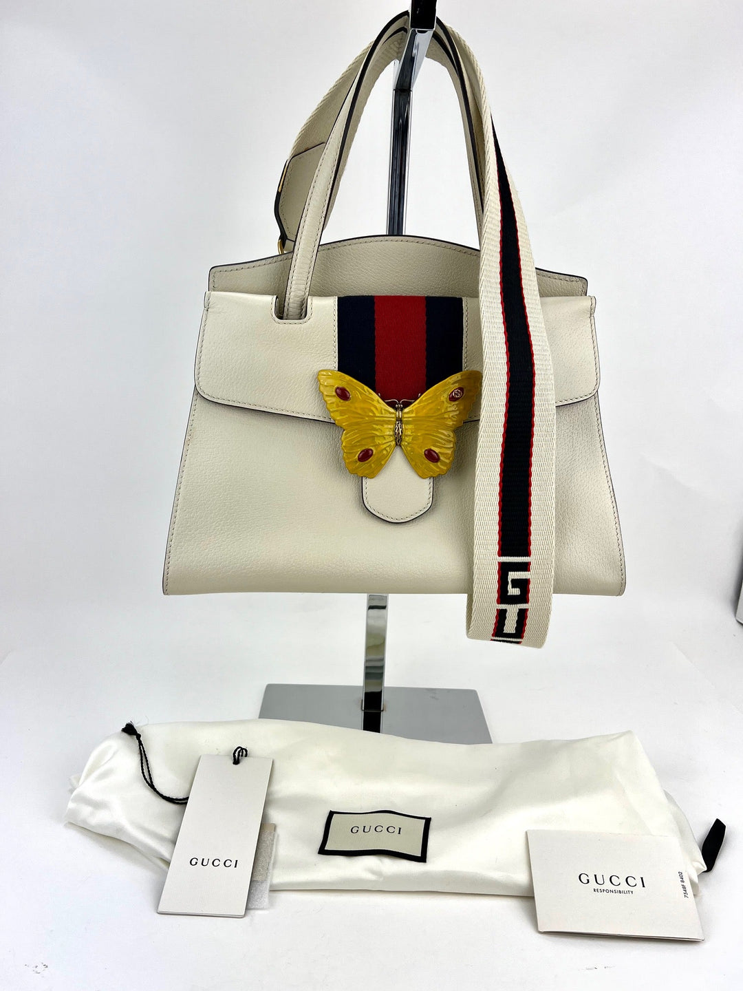 White handbag with butterfly design and Gucci strap on a white background