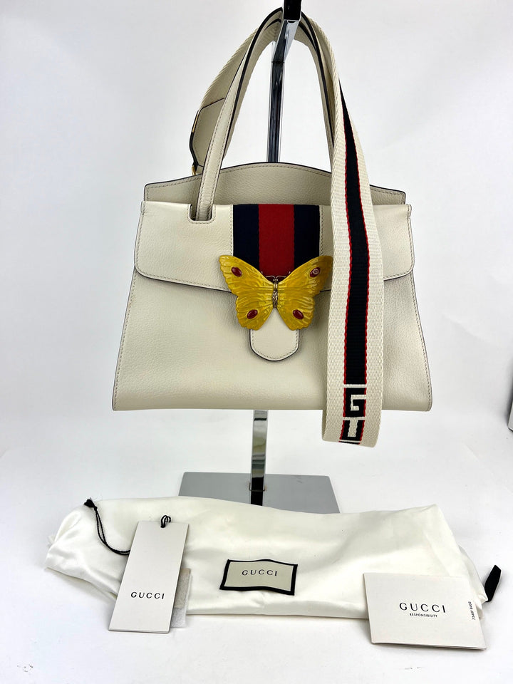 White handbag with butterfly design and Gucci strap on a white background