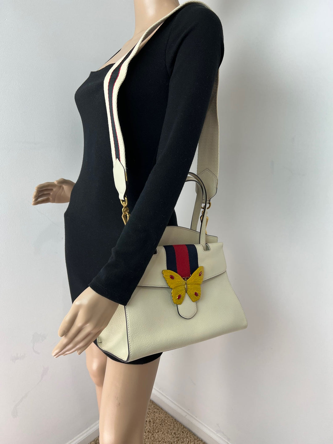 Mannequin wearing a black outfit with a white handbag featuring a butterfly design.