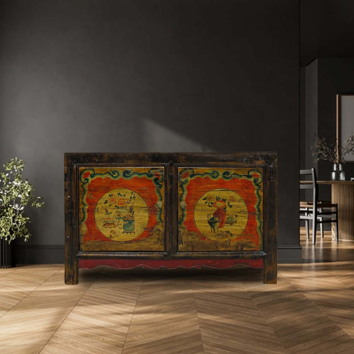 Decorative wooden cabinet with colorful artwork in a room with dark walls and wooden floor.