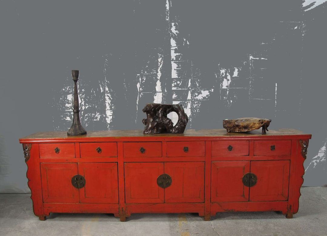 Red wooden sideboard with decorative items against a gray textured wall.