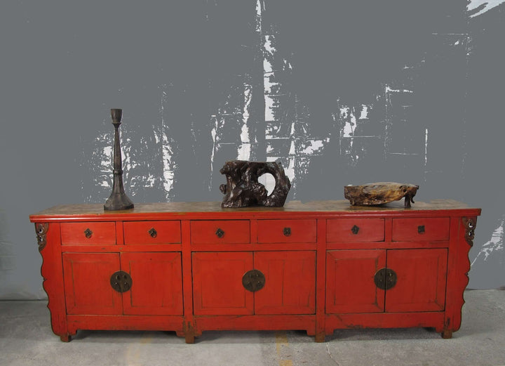 Red wooden sideboard with decorative items against a gray textured wall.