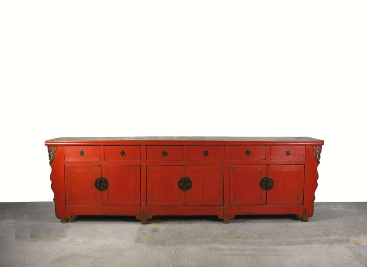 Red wooden dresser with black circular handles on a gray floor.