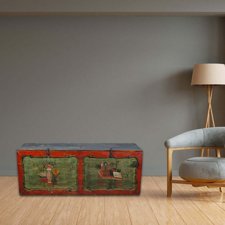 Vintage trunk with green and red paint in a modern room with a gray wall and wooden floor.