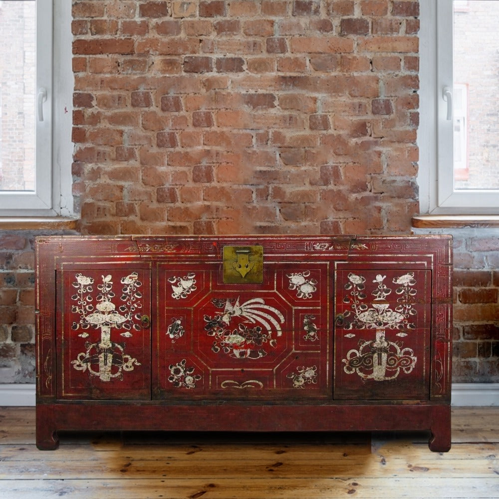 Decorative red chest with intricate patterns against a brick wall.