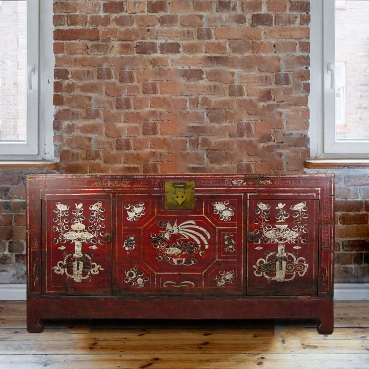 Decorative red chest with intricate patterns against a brick wall.
