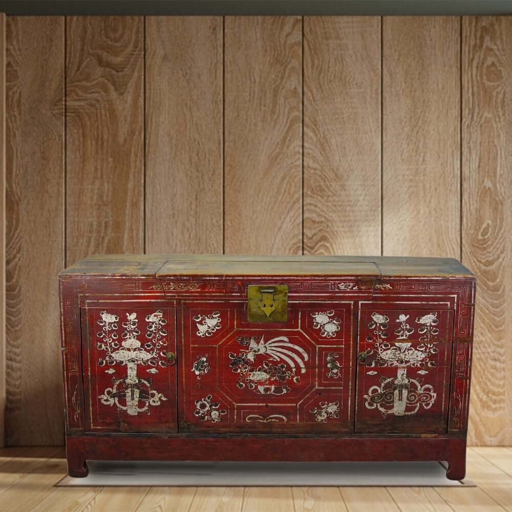 Red wooden chest with intricate designs against a wooden paneled wall.