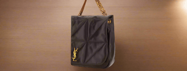 A brown leather Saint Laurent shoulder bag with a gold chain strap displayed in a store.
