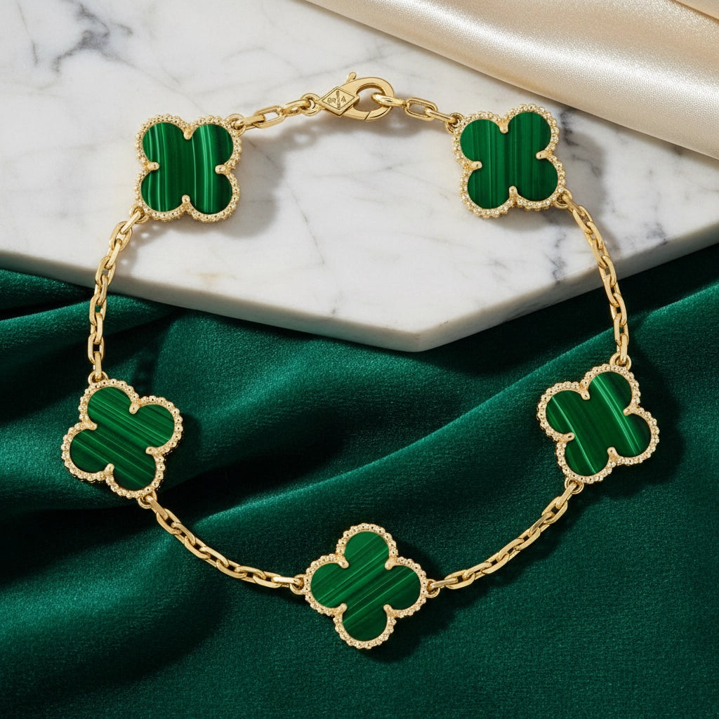 Gold bracelet with green clover-shaped charms on a marble and green fabric background