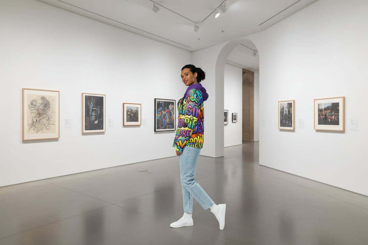 Model showcasing S7 Multicolor Inspiration Hoodie – Purple Edition in an art gallery, blending luxury fashion with creativity.