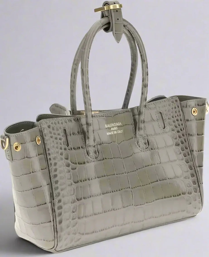 Gray crocodile-patterned handbag with gold accents on a white background