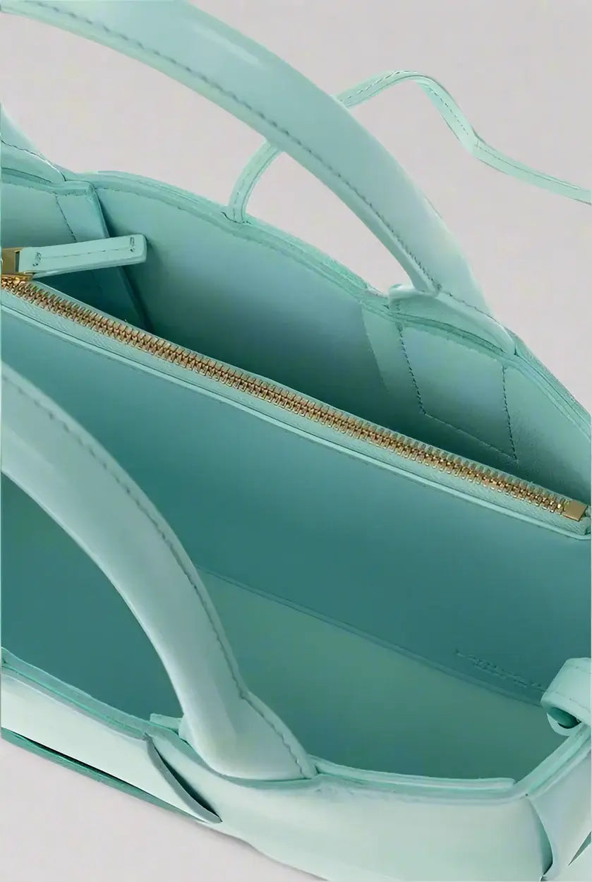 Close-up of a teal handbag with gold zipper on a white background