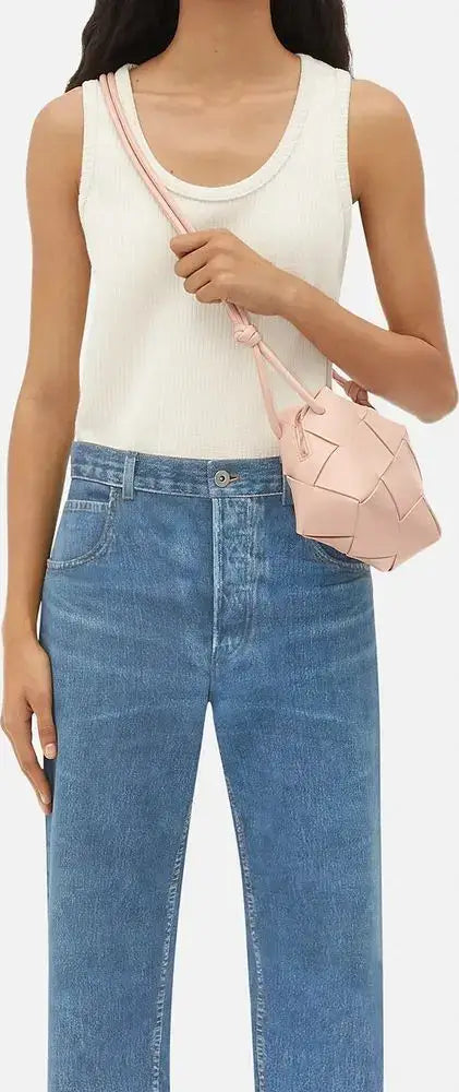 Person wearing a white tank top and blue jeans, holding a pink handbag.