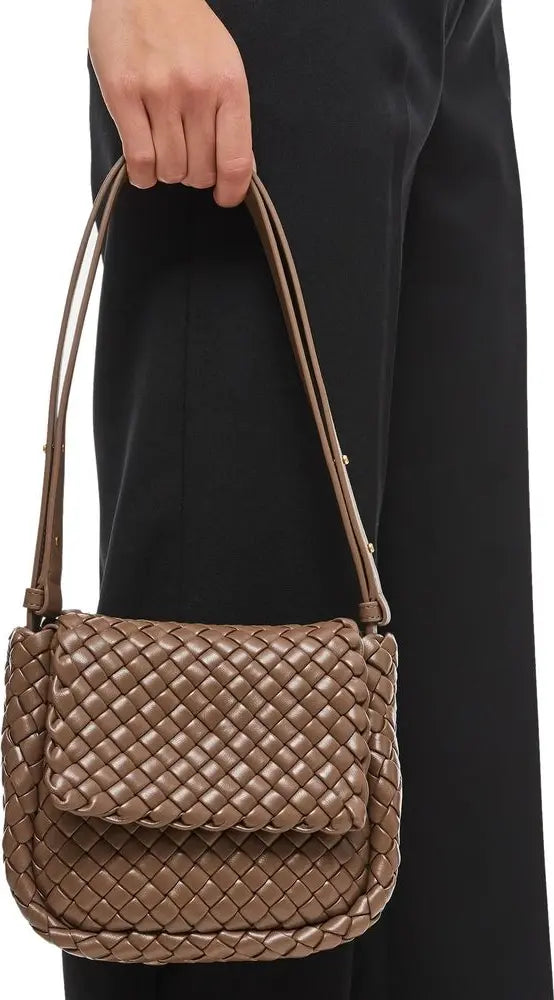Brown woven handbag held by a person wearing a black outfit.