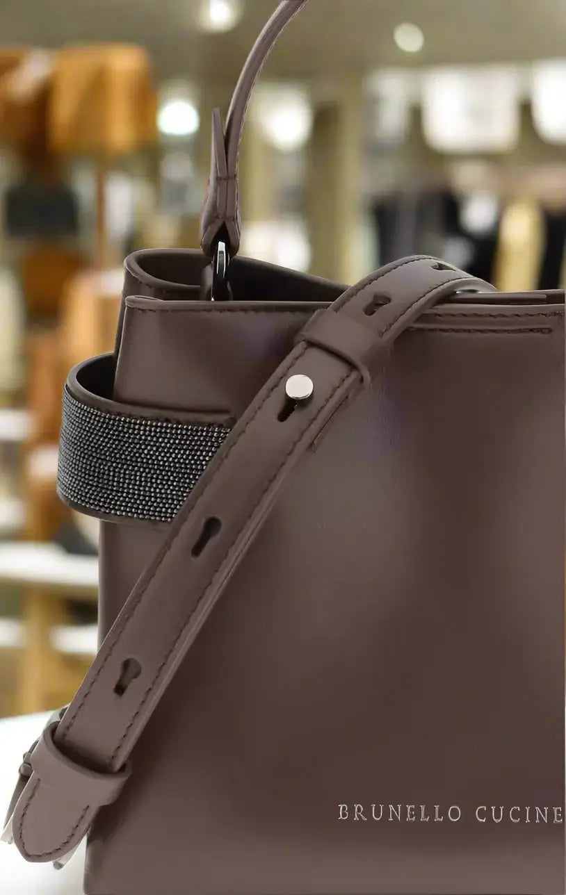Brown leather bag with a strap on a white background, featuring the Brunello Cucinelli brand.