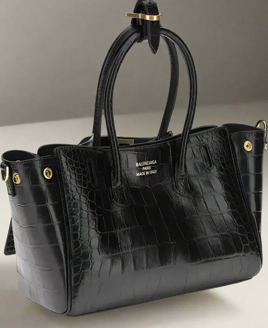 Black crocodile-patterned handbag with gold hardware on a white background