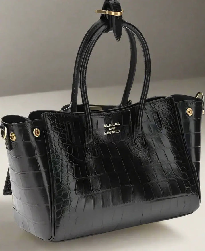 Black crocodile-patterned handbag with gold hardware on a white background