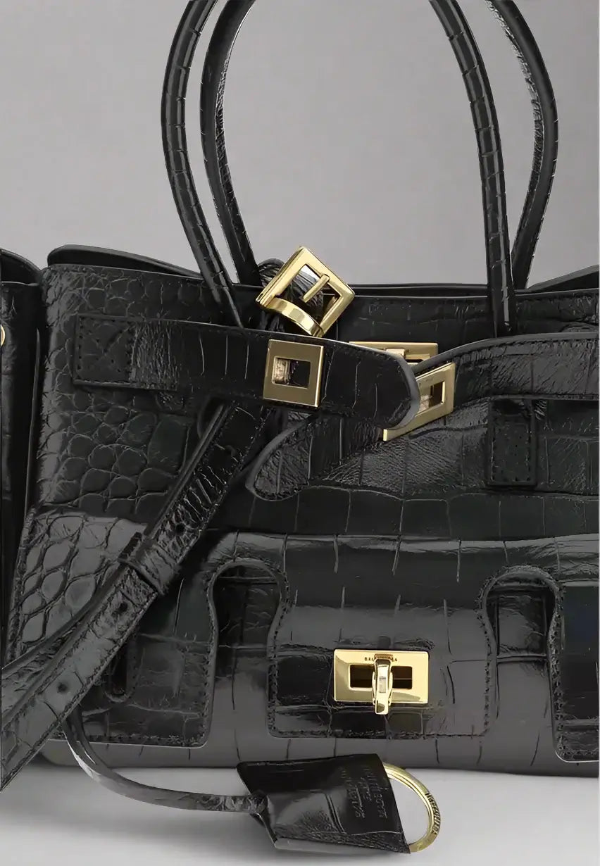 Black crocodile skin handbag with gold hardware on a white background