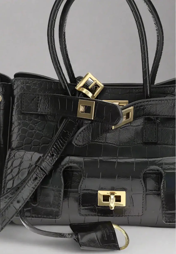 Black crocodile skin handbag with gold hardware on a white background