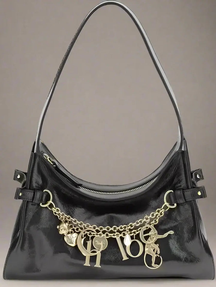 Black handbag with gold chain and charms on a white background