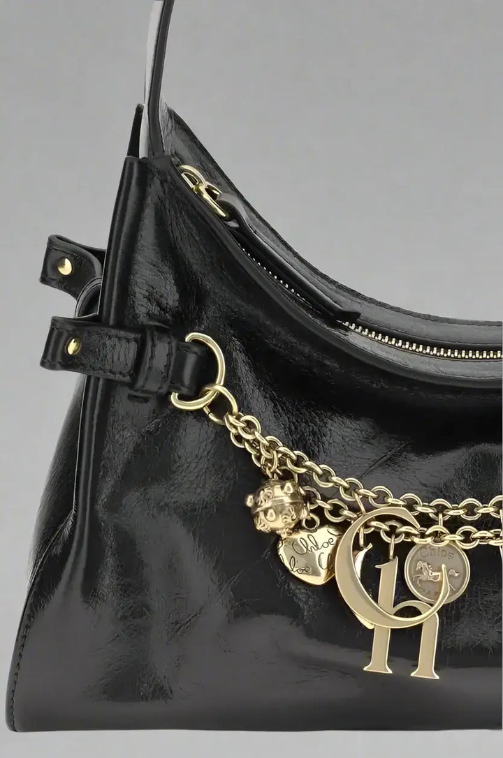 Black handbag with gold chain and charms on a white background