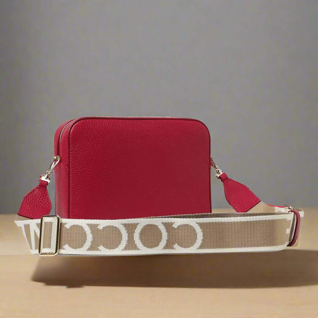 Red handbag with a beige and white patterned strap on a white background