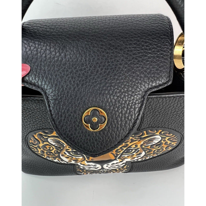 Black leather handbag with gold and silver decorative flap on a white background