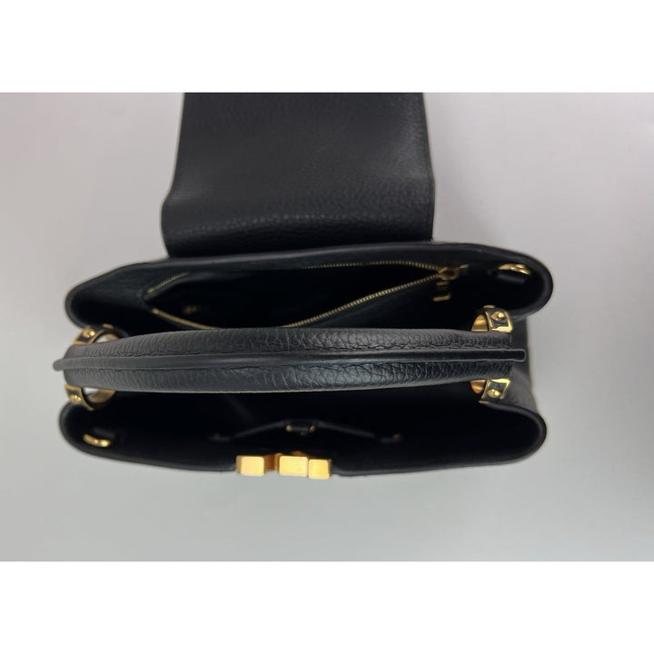 Black leather handbag with gold zippers on a light gray background