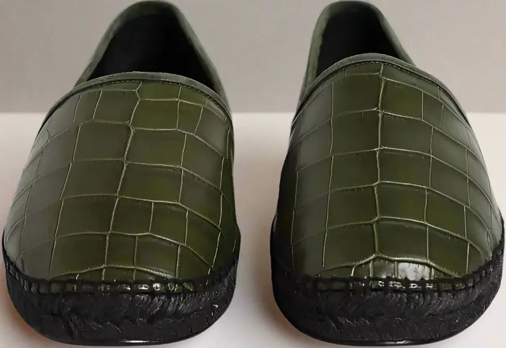 Pair of green crocodile-textured loafers on a white background