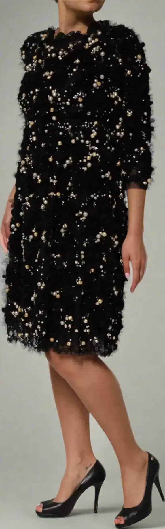Black dress with gold embellishments worn by a model on a white background