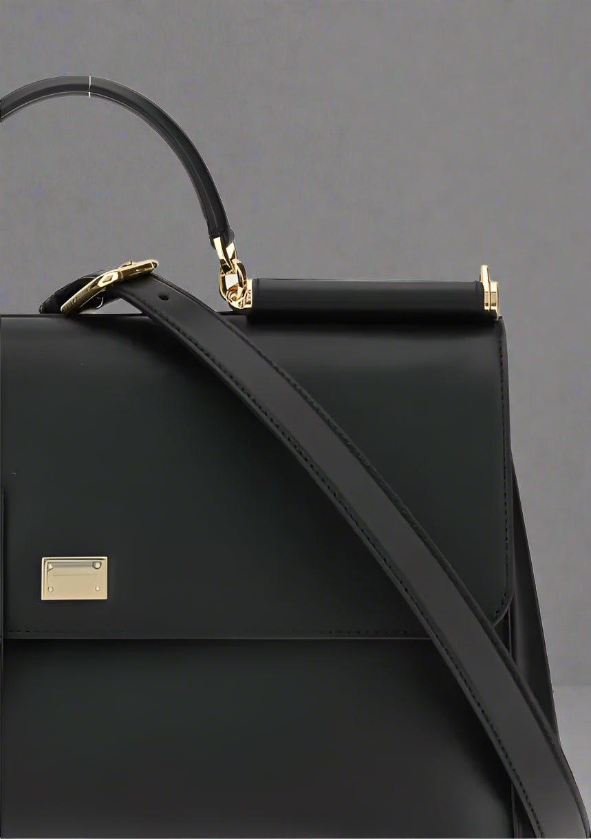 Black handbag with a gold clasp on a light gray background
