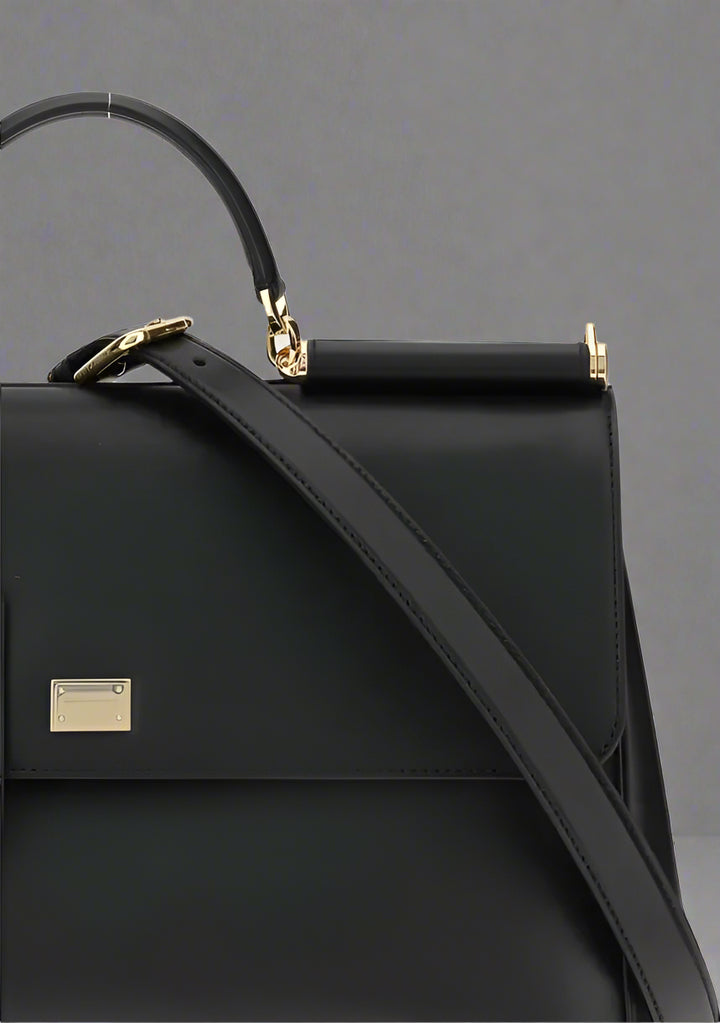 Black handbag with a gold clasp on a light gray background