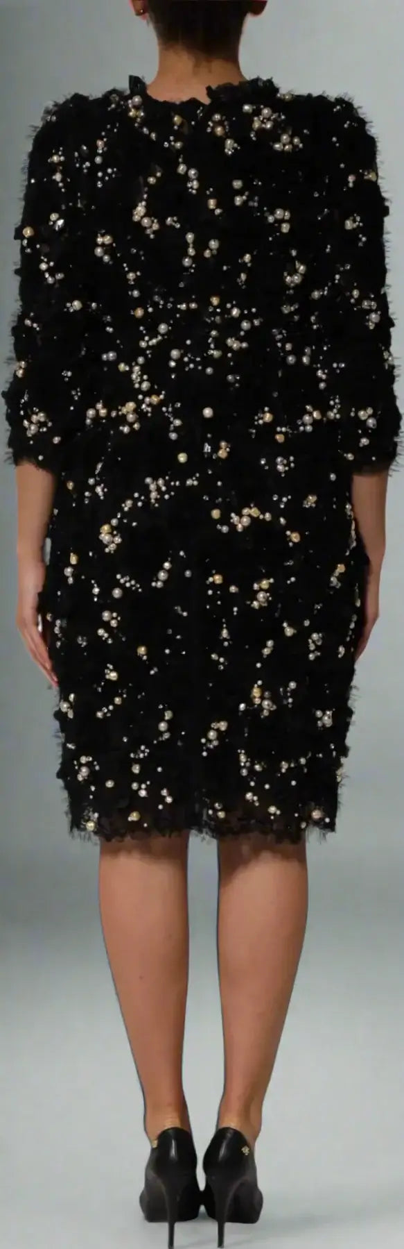 Black dress with gold sequins worn by a model on a white background