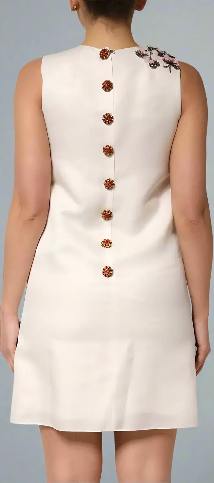 White sleeveless dress with brown buttons and floral details on a plain background