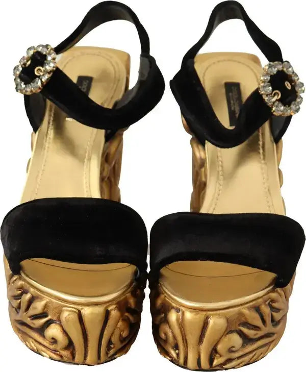 Pair of gold high-heeled sandals with black straps and decorative embellishments on a white background.