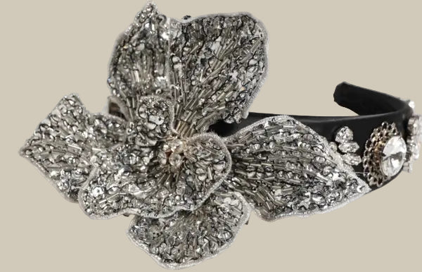 Decorative headband with silver flower and black band on a white background
