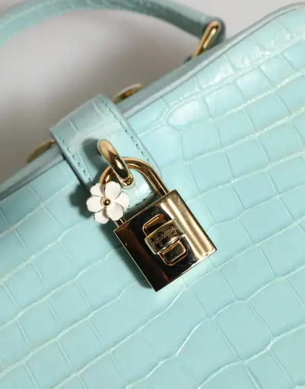 Light blue handbag with a gold lock and white flower charm on a light gray background