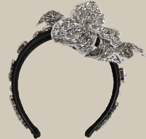 Decorative headband with a large bow and floral embellishments on a light gray background