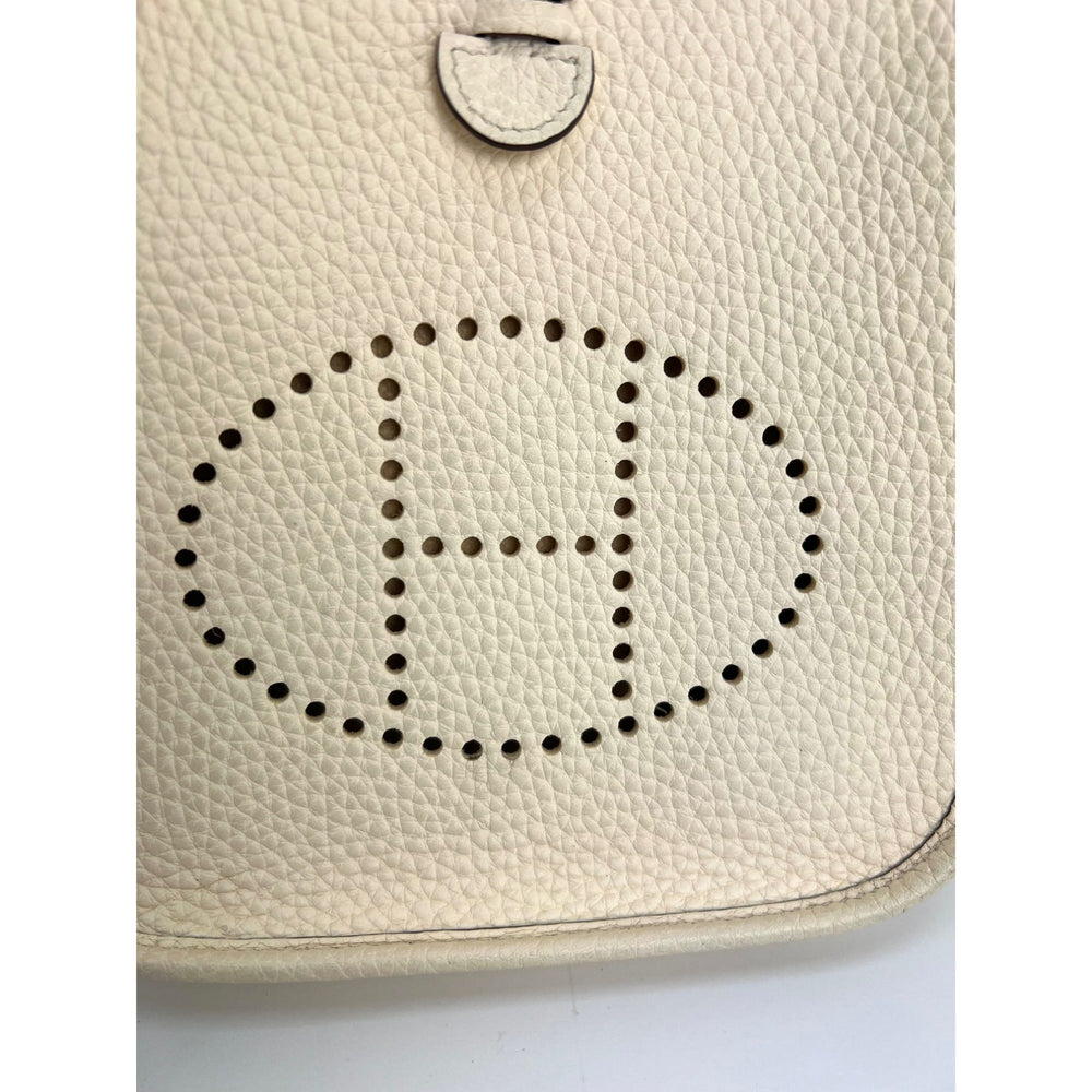 Close-up of a beige leather bag with a perforated 'H' logo on a white background