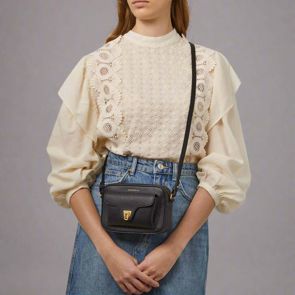 Person wearing a beige blouse with lace details and blue jeans, carrying a black crossbody bag.