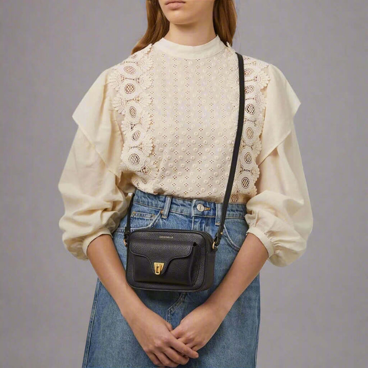 Person wearing a beige blouse with lace details and blue jeans, carrying a black crossbody bag.
