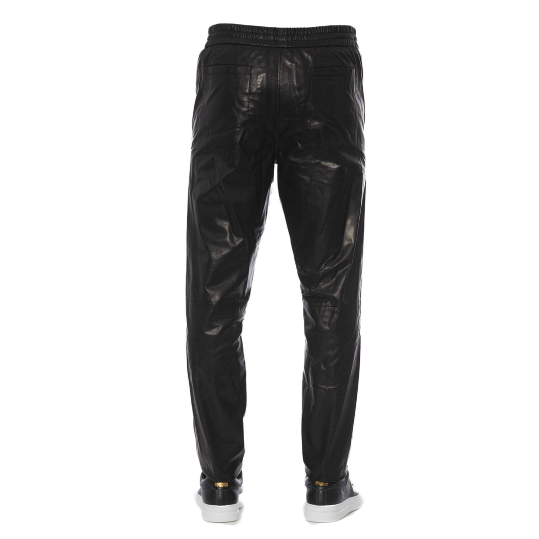 A pair of black Trussardi trousers with a visible logo, designed with two pockets, and a man standing in front wearing white sneakers.