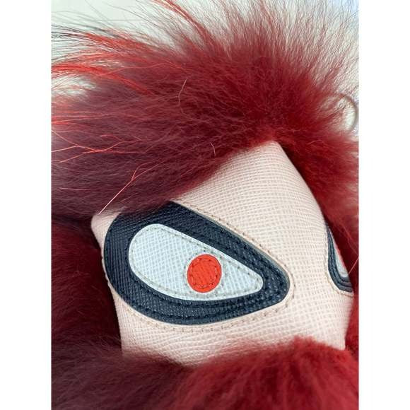 Close-up of a plush toy with red fur and a patch featuring an eye design on a white background