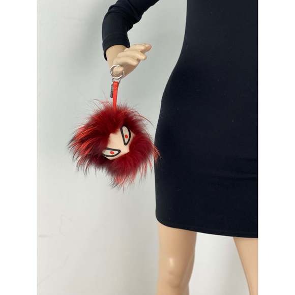 Red fluffy keychain held by a person wearing a black dress against a white background